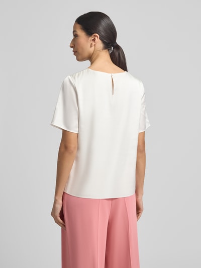 Frauenmodel trägt Regular Fit Bluse mit Rundhalsausschnitt und 1/2-Arm von Christian Berg Woman Selection, elfenbeinfarben, halbarm, Rückseite mit Knopfverschluss, zarter Material-Mix mit Stretch, kombiniert mit rosa Hose, glatte Struktur, Ganzkörperansicht Rückansicht.
