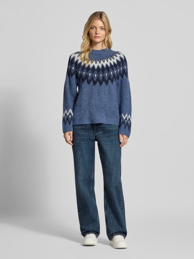 Vrouwenmodel draagt Relaxed Fit Pullover met wol-aandeel model 'Jacquard' van Gina Tricot, blauw-wit, gebreide textuur, ronde hals, strikpatroon, elastisch materiaal, vooraanzicht volledige lichaamsopname.