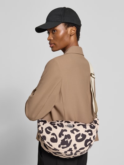 Frauenmodel trägt Umhängetasche mit Logo-Detail von Studio Noos im Allover-Animal-Print, beige-braun-schwarz, Ganzkörperansicht Rückansicht. Hauptfach mit Reißverschluss, verstellbarer Schulterriemen, Maße ca. 40x20x11 cm, Riemenlänge 65 cm.