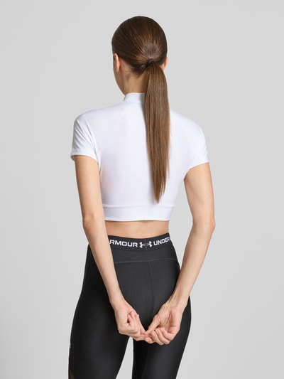 Frauenmodel trägt Cropped T-Shirt mit Logo und Stehkragen von Under Armour, weißer Material-Mix mit Stretch-Anteil, Rückenlänge 30 cm, Ganzkörperansicht Rückansicht.