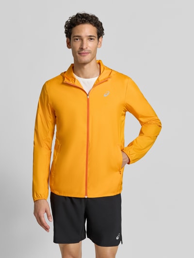 Männermodel trägt Regular Fit Trainingsjacke mit Logo-Print Modell 'Core' von ASICS TIGER in Orange, Kapuze, Reißverschluss, Ganzkörperansicht von vorne.