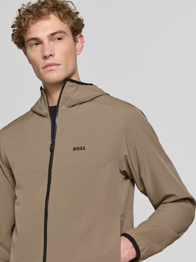 Mannelijk model draagt regular fit trainingsjack met capuchon model 'LW_COMMUTERPRO' van BOSS Green in beige, gladde textuur, nahaufnahme bovenlichaam.