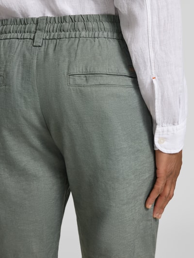Männermodel trägt Tapered Chinoshorts aus Leinen-Mix Modell 'DS_3S' von BOSS Orange in Grün mit elastischem Bund, Paspeltaschen, Nahaufnahme Rückansicht.