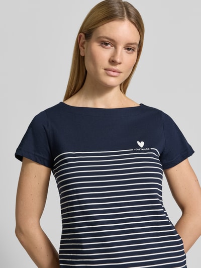Frauenmodel trägt Regular Fit T-Shirt aus reiner Bio-Baumwolle von Tom Tailor, dunkelblau mit weißen Streifen, Herz- und Label-Print, U-Boot-Ausschnitt, kurzarm; Nahaufnahme Oberkörper.