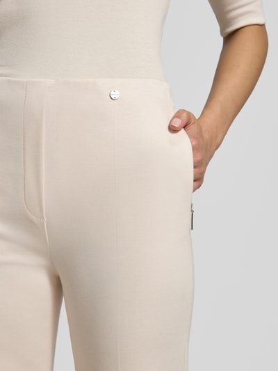 Frauenmodel trägt Stoffhose aus Viskose-Mix mit Bügelfalten von Marc Cain, cremefarben, elastischer Bund, Nahaufnahme Oberkörper.