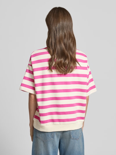 Frauenmodel trägt Oversized Fit Sweatshirt aus reiner Bio-Baumwolle Modell 'BAMIKAA' von Armedangels mit pink-weißen Streifen, Sweat-Material, Ganzkörperansicht Rückansicht.