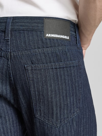 Männermodel trägt Tapered-Fit Jeans aus reiner Bio-Baumwolle Modell 'HERRINGBONE' von Armedangels, Denim-Optik, Label-Patch, Detailaufnahme.