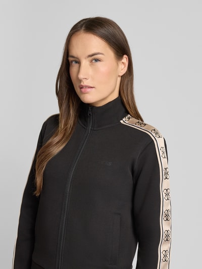 Frauenmodel trägt Regular Fit Sweatjacke mit Stehkragen Modell 'Britney' von Guess Activewear, Schwarz mit Logo-Detail, Nahaufnahme Oberkörper.