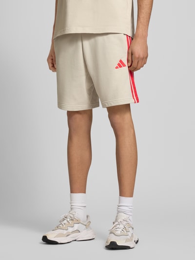Männermodel trägt Regular Fit Sweatshorts aus Baumwoll-Mix von adidas Sportswear, unifarben, Kontraststreifen, Nahaufnahme Unterkörper.