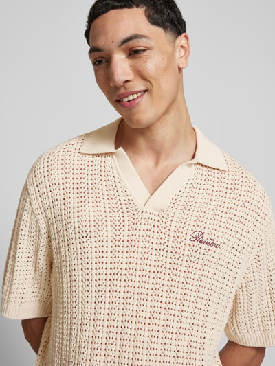Mannelijk model draagt Slim Fit Poloshirt in Crochet-Optik van REVIEW, katoen, polokraag, logo, beige tinten, detailopname bovenlichaam.