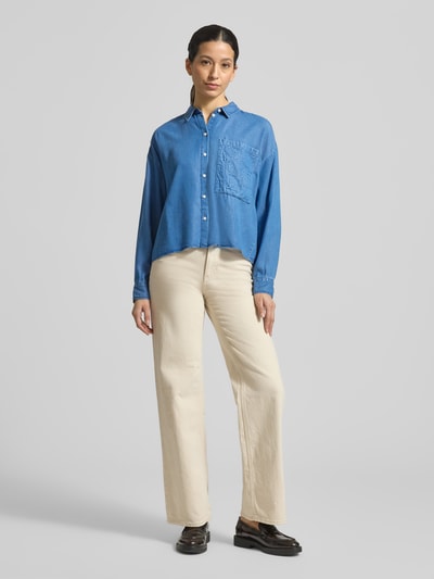 Frauenmodel trägt Boxy Fit Bluse aus Lyocell mit Label-Detail von Smith and Soul im Denim-Look, Hemdblusenkragen, Brusttasche, helle Hose, Ganzkörperansicht von vorne.