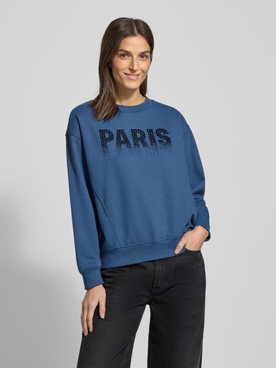 Frauenmodel trägt Regular Fit Sweatshirt aus Baumwoll-Mix von Tom Tailor Denim in Unifarbe Blau mit weichem Schriftzug-Print, Crew Neck, langarm, gerippte Abschlüsse, Ganzkörperansicht von vorne.