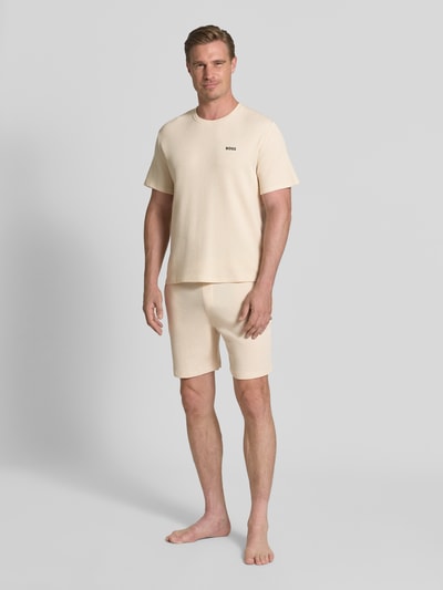 Männermodel trägt Regular Fit Sweatshorts aus Baumwoll-Mix von BOSS in Beige vor grauem Hintergrund, Ganzkörperansicht von vorne.