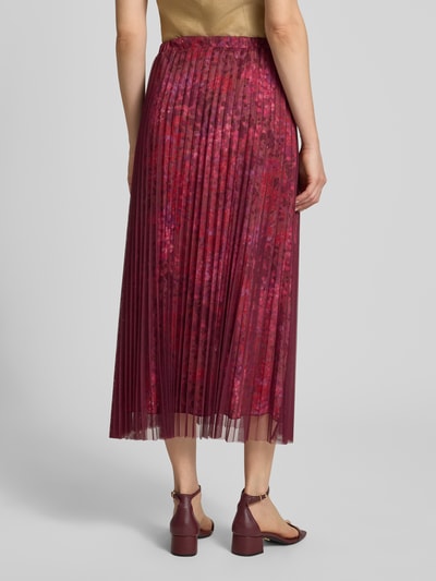 Frauenmodel trägt Midirock mit Plisseefalten im Allover-Look von Rich & Royal, bordeauxrot, Mesh, A-Linie, elastischer Bund, Ganzkörperansicht Rückansicht.