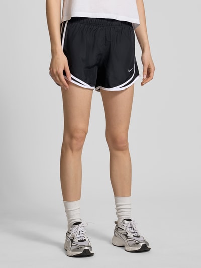Frauenmodel trägt Shorts mit Logo und elastischem Bund von NIKE TRAINING in Schwarz mit weißen Kontraststreifen, Regular-Fit, Ganzkörperansicht von vorne.