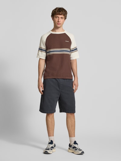 Männermodel trägt Shorts mit Gesäßtasche Modell 'Floyde' von Carhartt Work In Progress in Dunkelblau mit Loose Fit, Ganzkörperansicht von vorne. Lyocell-Mix, elastischer Bund und seitliche Eingrifftaschen ergänzen die strukturierte Optik.