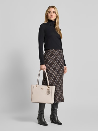 Frauenmodel trägt cremefarbene Handtasche mit Logo-Detail Modell 'NOELLE' von GUESS, Hauptfach mit Reißverschluss, schmale Schulterriemen, Ganzkörperansicht von vorne.