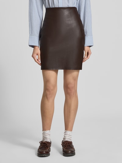 Frauenmodel trägt Minirock in Leder-Optik Modell 'DAGMAR' von VILA, körpernahe Passform, dunkelbraun, glatte Struktur, Ganzkörperansicht von vorne.