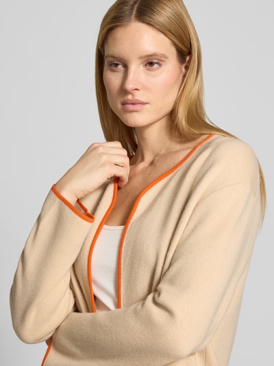 Frauenmodel trägt Strickmantel aus Baumwoll-Kaschmir-Mix mit aufgesetzten Taschen von HERZENS in Beige mit orangen Kanten, Nahaufnahme Oberkörper, Relaxed-Fit, offene Passform, Kontext: Rückenlänge bei Größe 36: 99 cm, Ärmellänge: 57 cm.