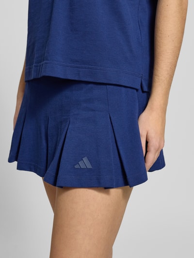 Frauenmodel trägt Ausgestellter Sportrock mit integrierten Tights von adidas aus reiner Baumwolle, tiefblau, Logo-Stitching, Nahaufnahme Oberkörper.