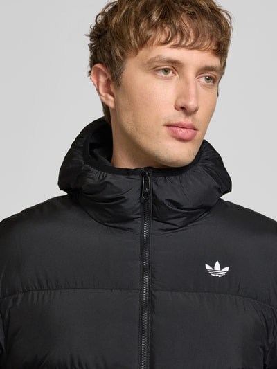 Männermodel trägt Regular Fit Steppjacke mit Logo-Detail von adidas Originals, unifarben schwarz, Popeline-Material, Nahaufnahme Oberkörper.