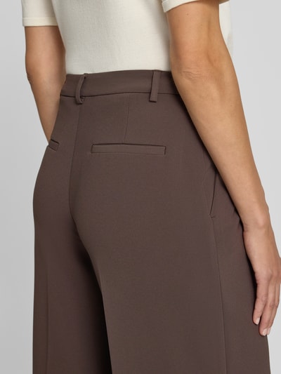 Frauenmodel trägt Wide Fit Hose mit Bundfalten von Rich & Royal in Braun, glatte Textur, Gesäßtaschen sichtbar, Nahaufnahme Rückansicht. Damen Hose, Bundweite 37 cm, Innenbeinlänge 80 cm.