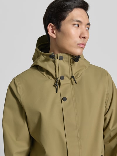 Männermodel trägt olivfarbene Regenjacke mit Kapuze, Kordelzug, verdecktem Verschluss, Label-Detail, Seitliche Reißverschlusstaschen, Produktname Regenjacke mit Reißverschlusstaschen Modell 'RAIN EATER' von GOFRANCK, glatte Oberfläche, Nahaufnahme Oberkörper.