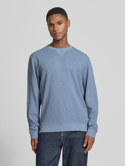Männermodel trägt Regular Fit Sweatshirt mit Rundhalsausschnitt von Scotch & Soda aus Baumwoll-Mix, Label-Detail, Ganzkörperansicht von vorne.