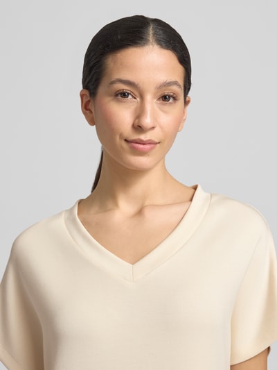 Modelka nosi T-Shirt-Kleid mit V-Ausschnitt od Soyaconcept, beżowy materiał z modalu, detal dekoltu, prosty krój, zbliżenie na górną część ciała.