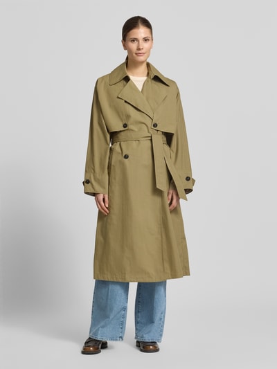 Vrouwenmodel draagt Trenchcoat met verdekte sluiting en strikceintuur van Blonde No. 8, katoenmix, getailleerd model, platte kraag, zij-steekzakken, knopen, kleur beige, gladde textuur, ruglengte maat 36 113 cm, schouderbreedte 60 cm, borstwijdte 54 cm, mouwlengte 49 cm, geheel aanzicht vooraan.