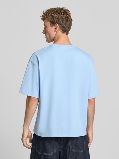 Męski model nosi t-shirt z wyhaftowanym logo i okrągłym dekoltem od REVIEW, bawełna, krój relaxed fit, długość tyłu w rozmiarze M: 69 cm, jasnoniebieski, gładka faktura, prostokątny fason. Ganzkörperansicht Rückansicht.