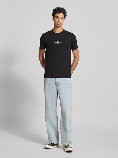 Männermodel trägt Regular Fit T-Shirt aus reiner Baumwolle Modell 'SIGN BLOCK' von Tommy Jeans, Optik: Unifarben, Schriftzug-Stitching, Label Print, Rücken-Print, Rundhals, Kurzarm, Material: reine Baumwolle, Ganzkörperansicht von vorne.