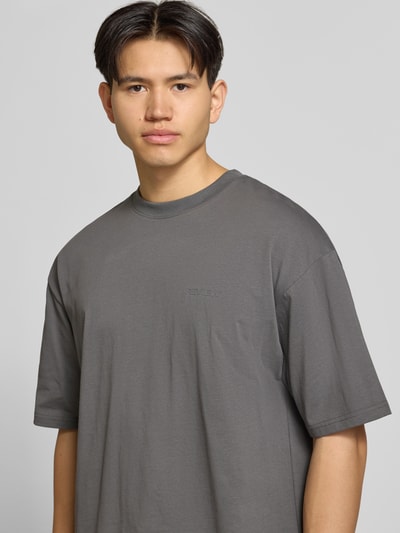 Mannenmodel draagt Oversized T-shirt met logo en ronde hals van REVIEW uit puur katoen in oversized fit, logoprint, ruglengte bij maat M 68 cm. Nahaufnahme Oberkörper.