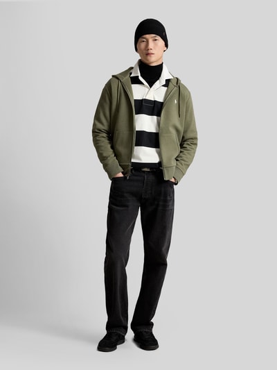 Mannenmodel draagt Regular Fit sweatjack van katoenmix van Polo Ralph Lauren in olijfgroen, zwarte jeans, wit-zwart gestreepte top, heren, full body aanzicht van voren.