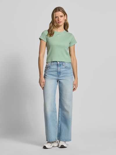 Frauenmodel trägt Cropped T-Shirt in Ripp-Optik mit Logo von Nike aus Baumwoll-Elasthan-Mix, Rundhalsausschnitt, Rückenlänge 50 cm, Ganzkörperansicht von vorne.