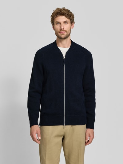 Männermodel trägt Regular Fit Strickjacke aus Baumwoll-Mix mit Kaschmir-Anteil von FTC Cashmere in Dunkelblau, Zweiwege-Reißverschluss, elastische Abschlüsse, College-Stil, Ganzkörperansicht von vorne.