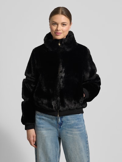 Frauenmodel trägt Jacke mit Teddyfell und gerippten Abschlüssen von Guess, schwarze Farbe, gerader Schnitt, Stehkragen, Reißverschluss, rippt an Bund und Ärmeln, Maße S: Rückenlänge 56 cm, Schulterbreite 38 cm, Brustweite 53 cm, Ärmellänge 61 cm, Ganzkörperansicht von vorne.