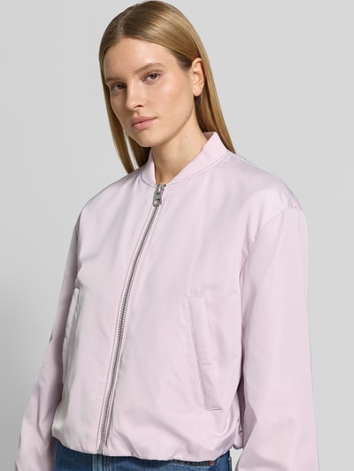 Modelka nosi Regular Fit Blouson mit Baseball-Kragen od Marc O'Polo, jednolity różowy, długie balonowe rękawy, elastyczne ściągacze, materiał recyklingowany, kieszenie boczne, zamek błyskawiczny, widok na górną część ciała z przodu.
