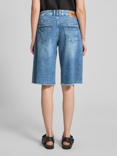 Frauenmodel trägt Jeansshorts mit Fransen Modell 'Rich' von MAC aus Baumwoll-Elasthan-Mix, Relaxed-Fit, Eingrifftaschen, Ganzkörperansicht Rückansicht.