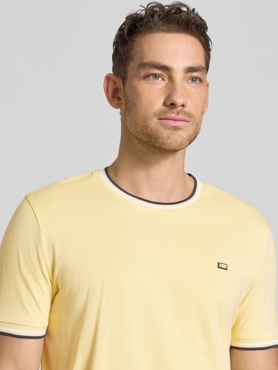 Męski model nosi T-Shirt mit Kontraststreifen und Rundhalsausschnitt von Christian Berg Men, mieszanka bawełny i elastanu, krój regular fit, paski w kontrastowym kolorze, okrągły dekolt, długość tyłu w rozmiarze M: 71 cm, jasny żółty, gładka faktura, detal logo, nahaufnahme górnej części ciała.