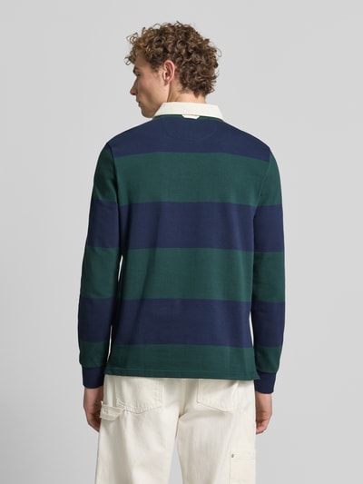 Männermodel trägt Poloshirt aus reiner Baumwolle von Christian Berg Men, grün-blaue Querstreifen, elastische Ärmelbündchen, lockere Passform, Rückenlänge 72 cm, Ärmellänge 67 cm, Ganzkörperansicht Rückansicht.