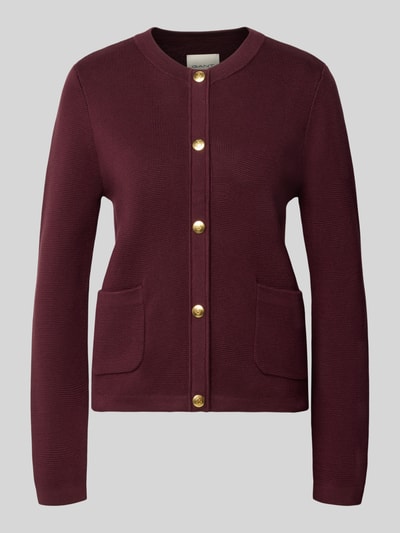Produktfoto, Regular Fit Strickjacke aus reiner Baumwolle von GANT in Dunkelrot mit goldfarbenen Knöpfen und aufgesetzten Taschen vor grauem Hintergrund.