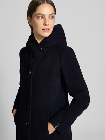 Vrouwenmodel draagt lange jas Model 'Bella' van Milo Coats van mix van scheerwol en kasjmier, regular fit, opstaande kraag, doorknoopsluiting, steekzakken, ruglengte maat 36: 93 cm, schouderbreedte: 43 cm, borstwijdte: 44 cm, mouwlengte: 64 cm, effen donkerblauw, gladde textuur, detailopname bovenlichaam.
