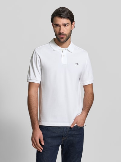 Męski model nosi Slim Fit Poloshirt mit Logo-Stitching od Gant, biała bawełna, krój slim fit, kołnierzyk polo, krótkie rękawy, widok całego ciała z przodu.