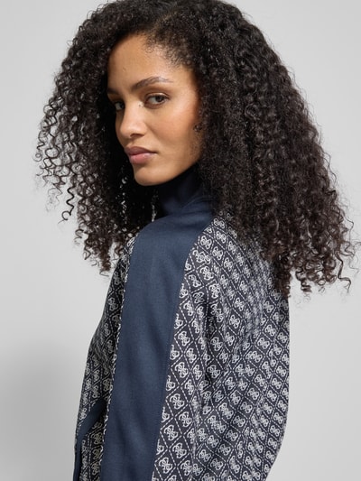 Männermodel trägt Sweatjacke mit Stehkragen Modell 'MAYA' von Guess Activewear w kolorze granatowym, wzór z logo, detal z przodu, Regular Fit, zbliżenie na górną część ciała, widok z przodu.