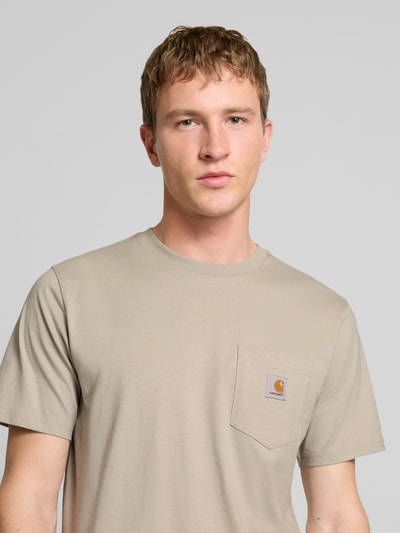 Männermodel trägt T-Shirt mit Label-Detail von Carhartt Work In Progress in Beige, reine Baumwolle, Regular Fit, Nahaufnahme Oberkörper.