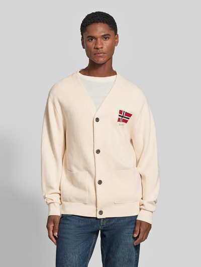 Männermodel trägt Cardigan mit Logo-Stitching Modell 'TARANGER' von Napapijri in Creme, Knopfleiste, Eingrifftaschen, Ganzkörperansicht von vorne. Reine Baumwolle, Regular Fit, V-Ausschnitt, Rückenlänge und Ärmellänge 68 cm bei Größe M.