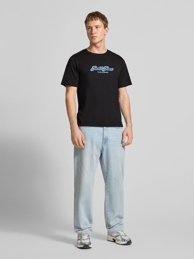 Männermodel trägt Regular Fit T-Shirt mit Logo-Print von Jack & Jones aus Reine Baumwolle, Rundhalsausschnitt, schwarze Farbe, Ganzkörperansicht von vorne.
