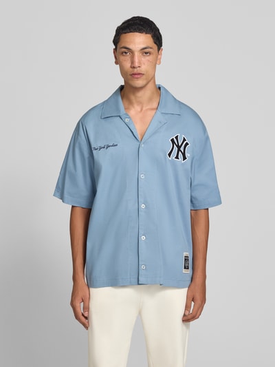 Männermodel trägt Relaxed Fit Freizeithemd aus Baumwoll-Mix von Champion in Hellblau mit Statement-Stitching, Reverskragen und kurzen Ärmeln, Ganzkörperansicht von vorne.