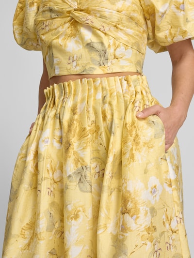 Frauenmodel trägt High Waist Midirock aus Lyocell-Mix Modell 'LEMON' von YAS mit gelbem Blumenmuster, Eingrifftasche, Drapierungen, Nahaufnahme Oberkörper.
